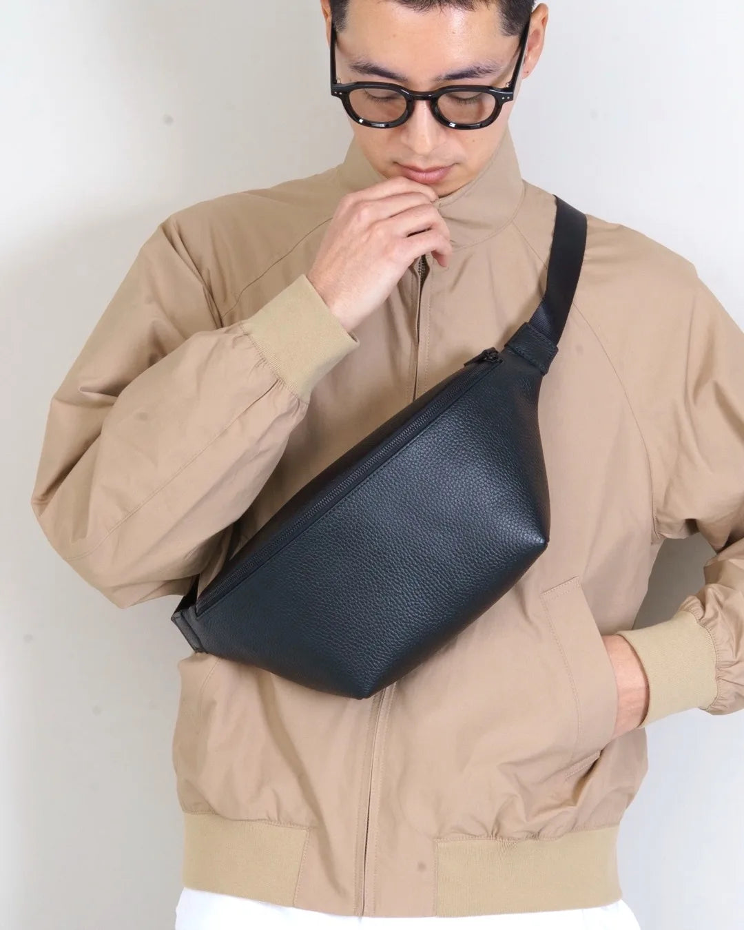 ジャケットの上からカーブドボディバッグを身につけた人